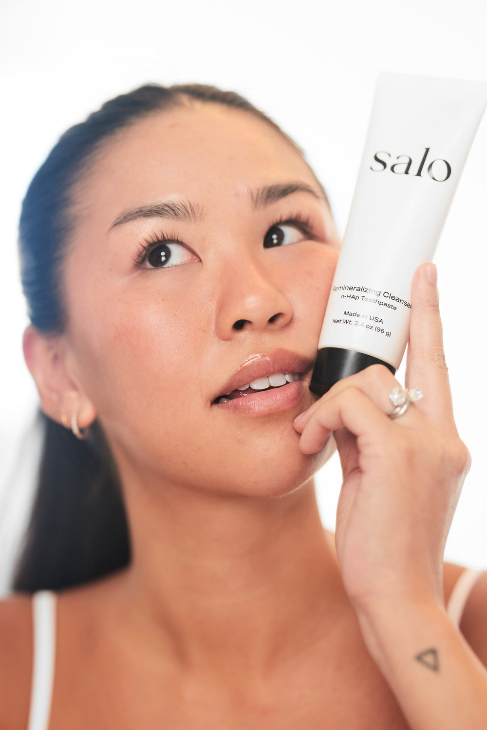Woman holding the Salo Remineralizing Cleanser tube beside her face