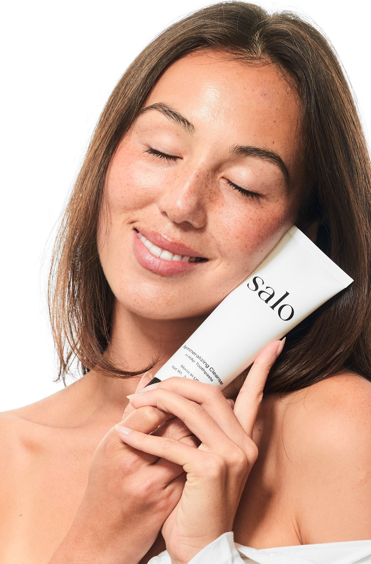 Woman holding the Salo Remineralizing Cleanser tube against her cheek